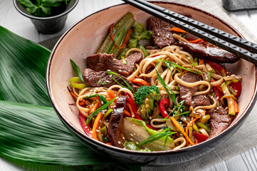 Udon stir fry noodles with beef meat and vegetables in a plate on white wooden background.