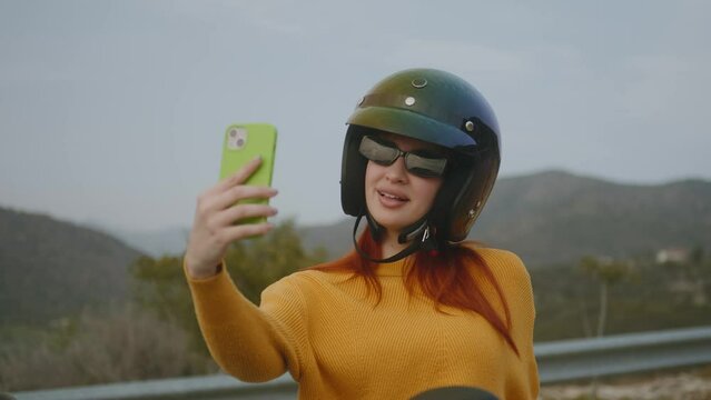 Happy woman taking selfies wearing motorbike helmet in nature, close-up
