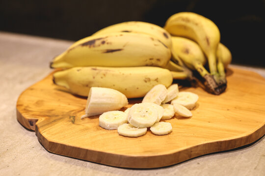 Banana picada com cacho de banana ao fundo sobre uma t&aacute;bua de madeira em fotografia macro.
