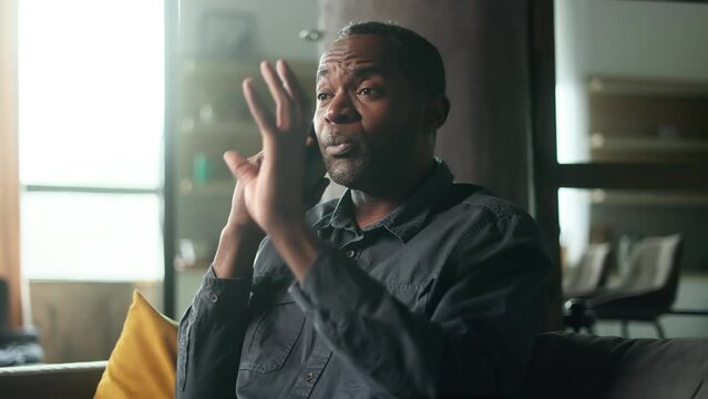 Irritated arguing mature african american man yelling at mobile phone on couch at home Angry nervous male talk on smartphone expressing negative emotion Bad conflict working or personal conversation