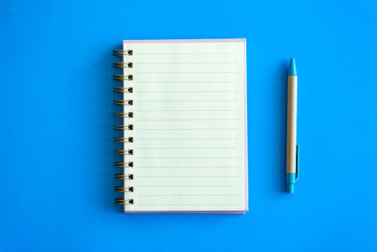 open notepad and craft pen next to it on a blue background. place for text. top view