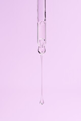 Glass pipette with facial serum and long falling drop on light purple background. Liquid skin care cosmetic product with bubbles closeup. Serum with retinol in droplet. Essential oil or gel macro.