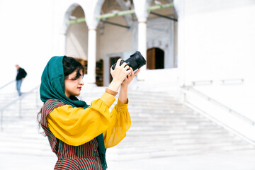 young Arab tourist woman wearing hijab, using camera during sightseeing in the city
