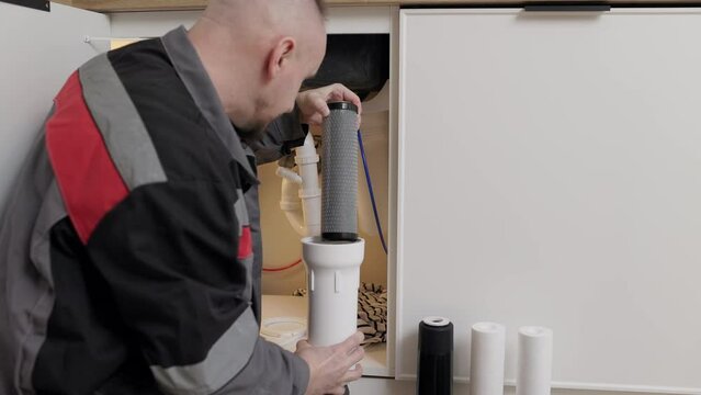 Repairman in overalls changes used drinking water set filters at the client kitchen. Installation of reverse osmosis water purification system. Concept Household filtration system. Service concept