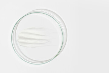 Petri dish on a light background. With a smear of white cream. Cosmetic cream, face mask, cream...