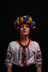 portrait of a girl in Ukrainian national clothes and jewelry with a wreath of blue and yellow flowers, blood on her face as a symbol of the war in Ukraine on a black background, vertical