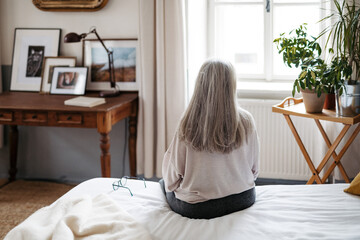 Rear view of senior woman sitting on a bed.