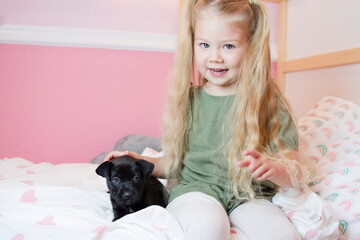 Little Caucasian little girl with a puppy. Child holding dog. Pet concept. Girl with pigtails with her puppy