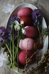 Naklejka na ściany i meble Happy Easter! A plate with naturally painted red and pink eggs with flowering spring flowers on rustic table.