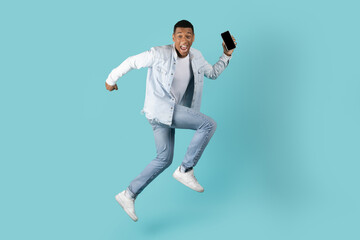 Fototapeta na wymiar Cheerful excited millennial black guy with open mouth running, jumping with smartphone, has fun