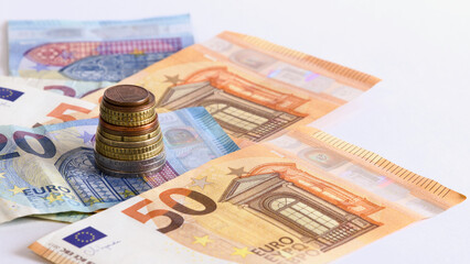 Stack of European Union euro coins over euro banknotes with a white background. Space for text