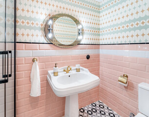 Retro colorful bathroom with wallpaper.  Mid Century pink and white tiles interior with vintage mirror, antique brass faucet and geometric op art floor