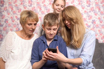Happy grandchildren, grandmother and mother have fun using smartphone.