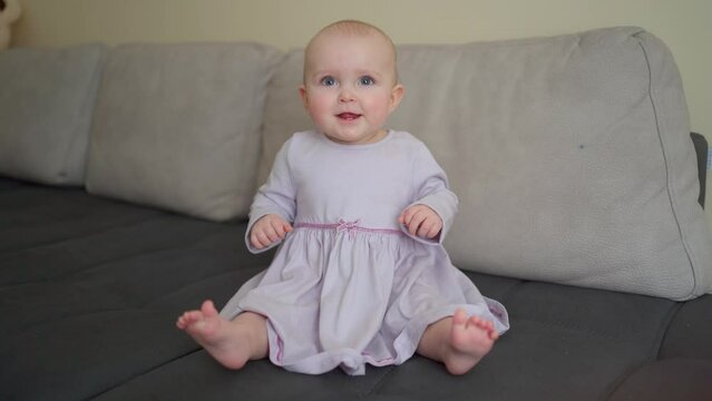 A cute little girl in a purple dress is sitting on the sofa and laughing .Mother's Day.