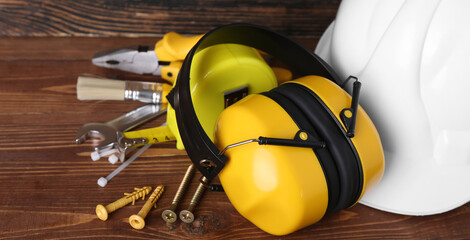 Hearing protectors with hardhat and tools on wooden background, closeup