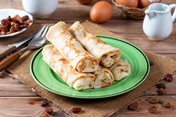Pancakes stuffed with cottage cheese and raisins on wooden table. A delicious sweet dessert