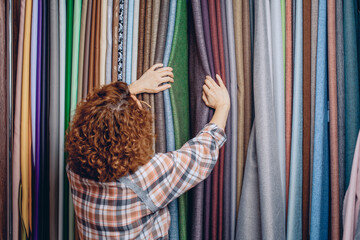 A seamstress girl stands in a fabric store and chooses the right material to create a new fashionable and high-quality product.