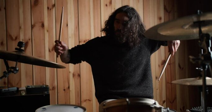 Male musician with drumsticks playing drums and cymbals with wooden wall on background