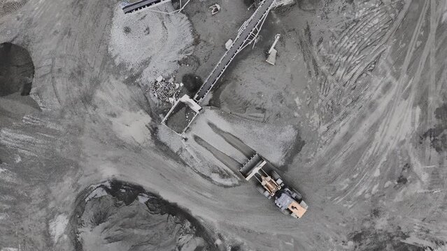 Truck pours gravel into sorter of conveyor system at mining quarry upper view. Granite material processing and transporting in pit
