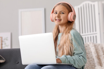 Little girl in headphones using laptop on sofa at home