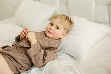 Portrait of a boy in a brown bathrobe, who is lying in bed, resting