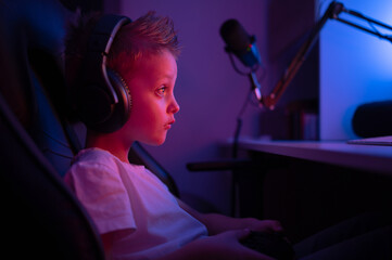 A little boy with headphones and a microphone plays computer games. Streams console games 