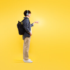 Guy With Backpack Touching Invisible Touchscreen Wearing Headphones, Yellow Background