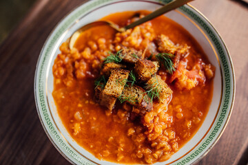 red lentil and tomato soup with fennel and croutons in white bowl with green greek key and golden spoon