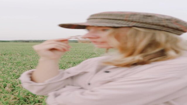 A blonde in a cap walks in a rice field holding a rice ear to her lips