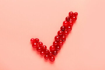 Check mark made of lingonberries on pink background
