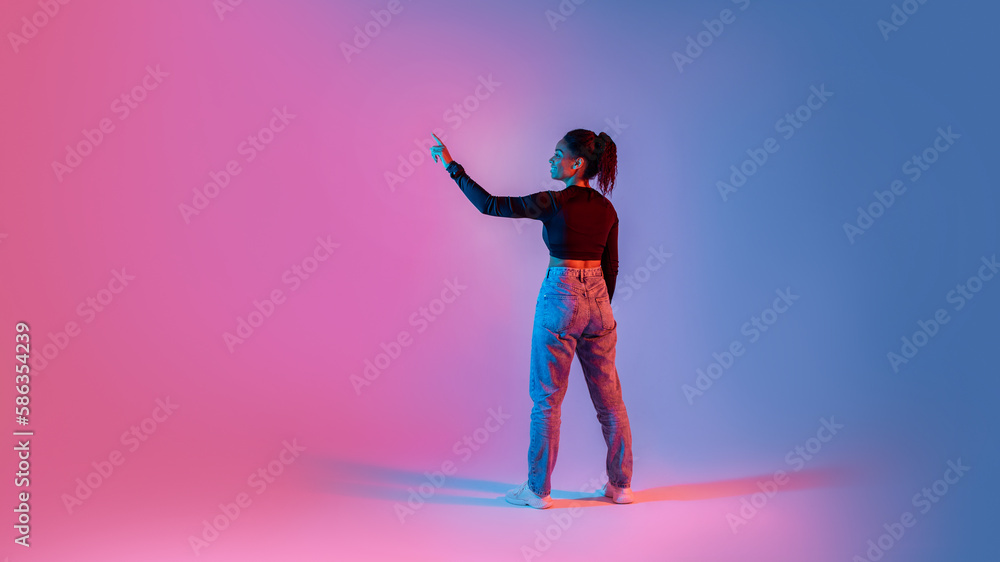 Aufkleber back view of black lady touching imaginary screen, using virtual interface on colorful neon backgrou