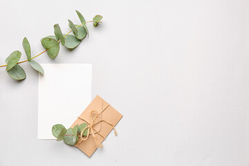 Composition with blank card, envelope and eucalyptus branches on white background