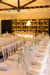 Served wedding table with decorative fresh white flowers and candles. Celebration details. Hanging flower beds and light bulbs Wedding decoration and decor, floristic concept