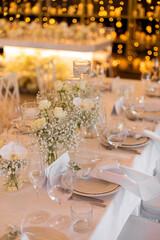 Served wedding table with decorative fresh white flowers and candles. Celebration details. Hanging flower beds and light bulbs Wedding decoration and decor, floristic concept