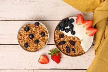 Bowls of tasty granola with yogurt and berries on light wooden background