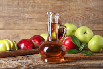 Glass bottle of fresh apple cider vinegar and board with fruits on wooden table