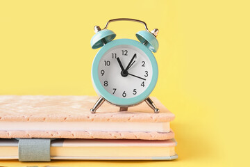 Notebooks and alarm clock on yellow background