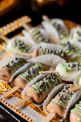 Close up of sweets on a golden plate from a wedding candy bar. Summer chocolate popsicles covered with green icing