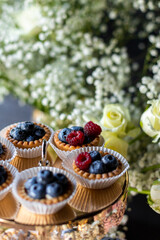Close up of sweets on a golden plate from a wedding candy bar. Tartlets with summer berries: blueberries and raspberries