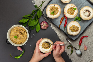 Female hands stuff raw mushroom caps. Fresh champignons ready for baking, spices, vegetables