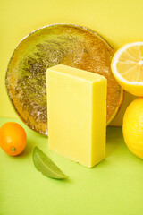Composition with natural soap bar, golden plate and citrus fruits on color background, closeup