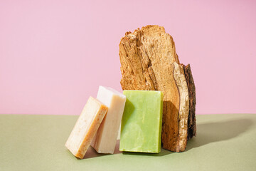 Natural soap bars and tree bark on color background