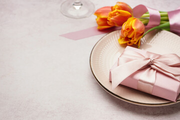Clean plate, gift box, tulip flowers and wine glass on white grunge table