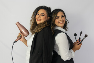 Two women from the back, one holding a hair dryer and the other makeup brushes