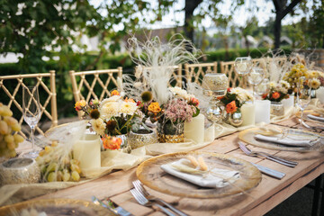 Wedding decorations. Served wedding table with golden plates, napkins, decorative fresh and dried flowers, candles and and light bulbs. Celebration details, wedding outdoor	
