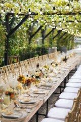 Wedding decorations. Served wedding table with golden plates, golden chairs, napkins, decorative fresh and dried flowers, candles and light bulbs. Celebration details, wedding outdoor	
