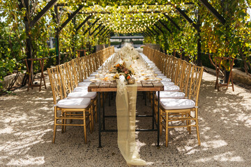 Wedding decorations. Served wedding table with golden plates, golden chairs, napkins, decorative fresh and dried flowers, candles and light bulbs. Celebration details, wedding outdoor	
