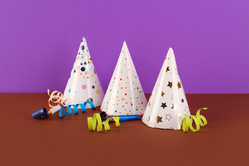 Party hats, whistles and serpentine on color background