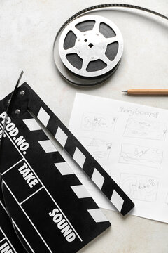 Movie clapper with storyboard and film reel on light background