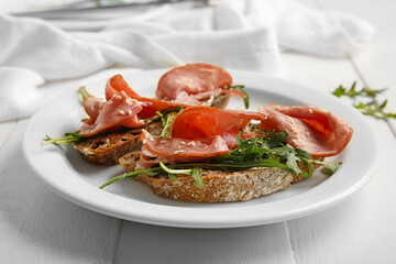 Plate of tasty bruschettas with ham on white wooden background